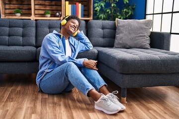 Wall Mural - African american woman listening to music sitting on floor at home