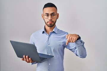 Wall Mural - Young hispanic man working using computer laptop pointing down looking sad and upset, indicating direction with fingers, unhappy and depressed.