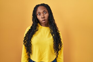 Wall Mural - African woman standing over yellow background making fish face with lips, crazy and comical gesture. funny expression.