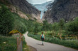 Woman hiking along path to Briksdalsbreen glacier in the mountains of Jostedalsbreen national park in Norway, green meadows with flowers in foreground