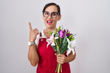 Poster - Middle age brunette woman wearing apron working at florist shop holding bouquet pointing finger up with successful idea. exited and happy. number one.