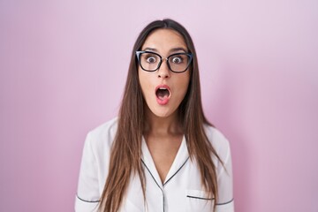 Poster - Young brunette woman wearing glasses standing over pink background afraid and shocked with surprise expression, fear and excited face.