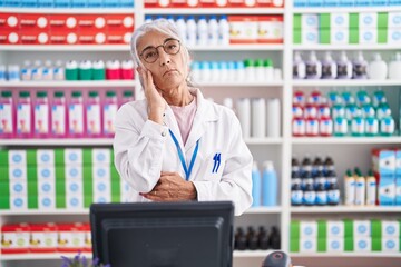 Wall Mural - Middle age woman with tattoos working at pharmacy drugstore thinking looking tired and bored with depression problems with crossed arms.