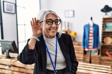 Poster - Middle age grey-haired woman working as manager at retail boutique smiling with hand over ear listening an hearing to rumor or gossip. deafness concept.