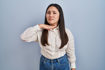 Poster - Young latin woman standing over blue background cutting throat with hand as knife, threaten aggression with furious violence