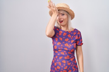 Poster - Young caucasian woman wearing flowers dress and summer hat surprised with hand on head for mistake, remember error. forgot, bad memory concept.