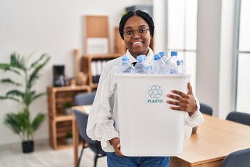 Canvas Print - African american woman working at the office holding plastic bottle for recycling smiling with a happy and cool smile on face. showing teeth.