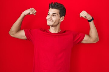 Canvas Print - Young hispanic man standing over red background showing arms muscles smiling proud. fitness concept.