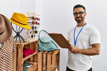 Sticker - Young hispanic man shopkeeper writing on checklist working at clothing store