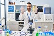 © Krakenimages.com - Young hispanic man with beard working at scientist laboratory showing and pointing up with fingers number ten while smiling confident and happy.
