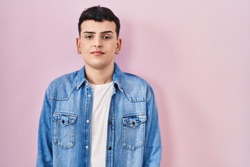 Poster - Non binary person standing over pink background with serious expression on face. simple and natural looking at the camera.