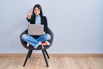 Poster - Young hispanic woman sitting on chair using computer laptop pointing with finger up and angry expression, showing no gesture