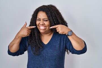 Sticker - Plus size hispanic woman standing over white background smiling cheerful showing and pointing with fingers teeth and mouth. dental health concept.