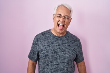 Wall Mural - Middle age man with grey hair standing over pink background sticking tongue out happy with funny expression. emotion concept.