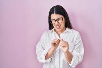 Poster - Young brunette woman standing over pink background disgusted expression, displeased and fearful doing disgust face because aversion reaction. with hands raised