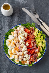 Wall Mural - Tradition Cobb salad with fried chicken, avocado, fresh tomatoes, eggs, bacon and cheese on a plate on a dark background. Top view, copy space, selective focus