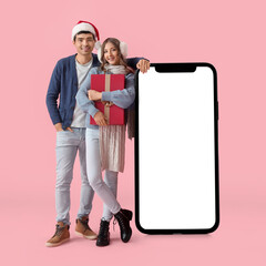 Sticker - Young couple with Christmas gift and big smartphone on pink background