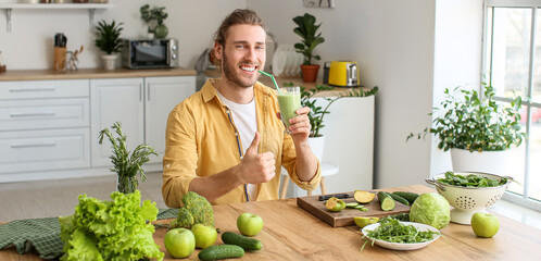 Young man drinking healthy green smoothie in kitchen