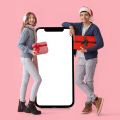 Poster - Happy young couple with Christmas gifts and big smartphone on pink background