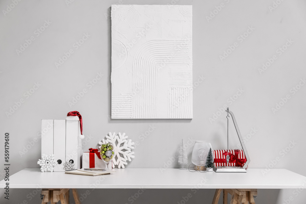 Folders with Santa hat, lamp and Christmas decor on table near light wall