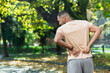 © Liubomir - Tired man after jogging in park, hispanic man has severe pain in back and muscles after fitness, massaging his side with hand near trees.