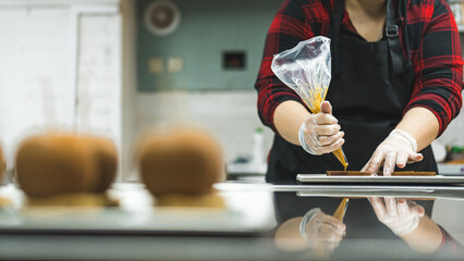 Unrecognizable pastry chef using pastry bag - sac a poche - in bakery kitchen. Copy space. Blurred foreground with sweets. High quality photo