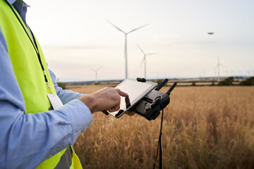 Wall Mural - Operator holding remote control and quadcopter. Unmanned aerial copter starting in wind field. Male operating a drone using a remote controller. Engineer playing with drone renewable energy control