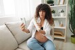 © SHOTPRIME STUDIO - Pregnant woman smile blogger showing baby feeding bottle filming herself on phone, video chat sitting on sofa at home freelancer in last month of pregnancy