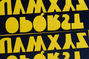 Poster - reversed and flipped stencils with alphabet letter cutouts on grungy yellow corrugated paper