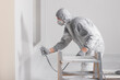 © New Africa - Decorator in protective overalls painting wall with spray gun indoors