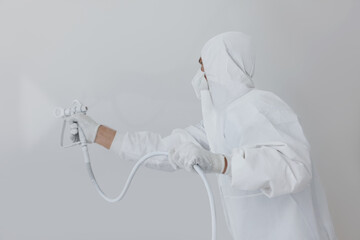 Wall Mural - Decorator in uniform painting white wall with spray