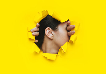 Wall Mural - Female ear and two hands close-up. Copy space, torn paper and yellow background. The concept of eavesdropping, espionage, gossip and the yellow press.