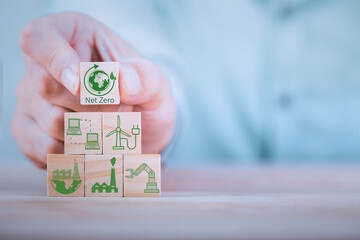 Wall Mural - Businessman hand arranging wood block with net zero icon , Net zero by 2050 Carbon neutral energy or Net Zero greenhouse gas emission target on wooden cubes background