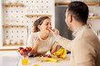 © dusanpetkovic1 - A man is feeding his wife with apple at home in kitchen.
