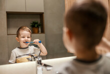 A Little Boy Is Standing In Front Of The Mirror And Brushing His Teeth In The Bathroom.
