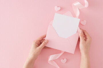 Women day celebration concept. First person top view photo of girl holding envelope with letter over silk ribbon and hearts baubles on pink background with copy space. Mothers day holiday card idea.