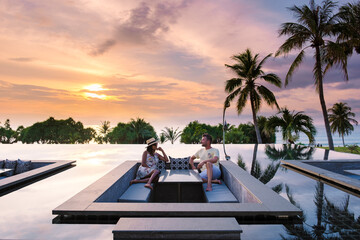 Wall Mural - couple watching the sunset in an infinity pool on a luxury vacation in Thailand, man and woman watching the sunset on the edge of a pool in Thailand on vacation