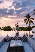 Couple Watching The Sunset In An Infinity Pool On A Luxury Vacation In Thailand, Man And Woman Watching The Sunset On The Edge Of A Pool In Thailand On Vacation