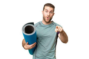 Poster - Young sport man going to yoga classes while holding a mat over isolated chroma key background surprised and pointing front