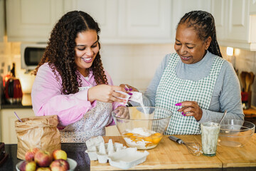 Wall Mural - African mother and daughter preparing fruit cake at home - Soft focus on girl face