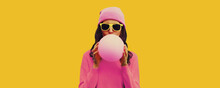 Fashionable Portrait Of Stylish Cool Young Woman Inflating Chewing Gum Or Balloon Wearing Pink Hat On Yellow Background, Blank Copy Space For Advertising Text