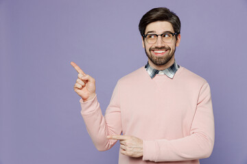 Wall Mural - Young happy IT man he wear casual clothes pink sweater glasses point index finger aside indicate on workspace area copy space mock up isolated on plain pastel light purple background studio portrait.