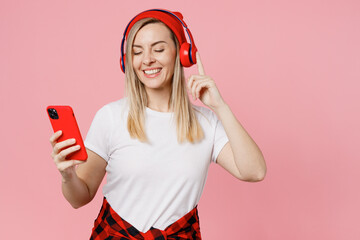 Wall Mural - Young fun happy woman wear white t-shirt red hat headphones listen to music use mobile cell phone close eyes isolated on plain pastel light pink background studio portrait. People lifestyle concept.