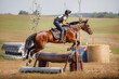 close portrait of attractive rider woman jumping over obstacle on bay mare horse during eventing cross country competition in summer