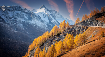 Fotobehang - Incredible autumn landscape during sunset. Scenic view on mountain highland with colorful trees and perfect blue sky in the background the beautiful Grossglockner. Amazing nature background. postcard