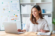 © amnaj - Beautiful Asian businesswoman using her laptop enjoying work, taking notes, reviewing work done.