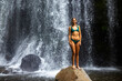 beautiful girl in a bikini standing under a tropical waterfall in Costa Rica; swimming in a hidden waterfall in the rainforest