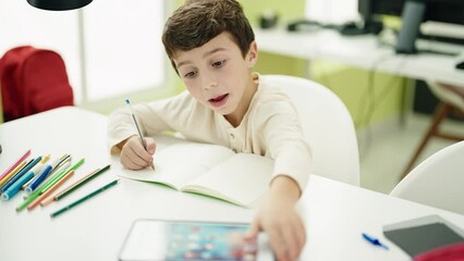 Poster - Adorable hispanic boy student using touchpad writing on notebook at classroom