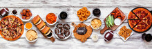 Super Bowl Or Football Theme Food Table Scene. Pizza, Hamburgers, Wings, Snacks And Sides. Top Down View On A White Wood Background.