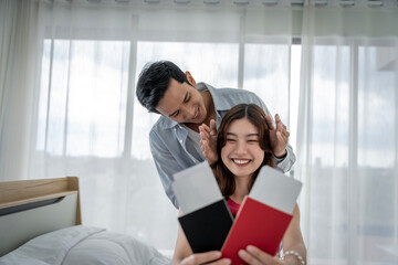 Wall Mural - Asian couple surprises girlfriend with plane ticket and passport to hang out together on vacation in their bedroom at home